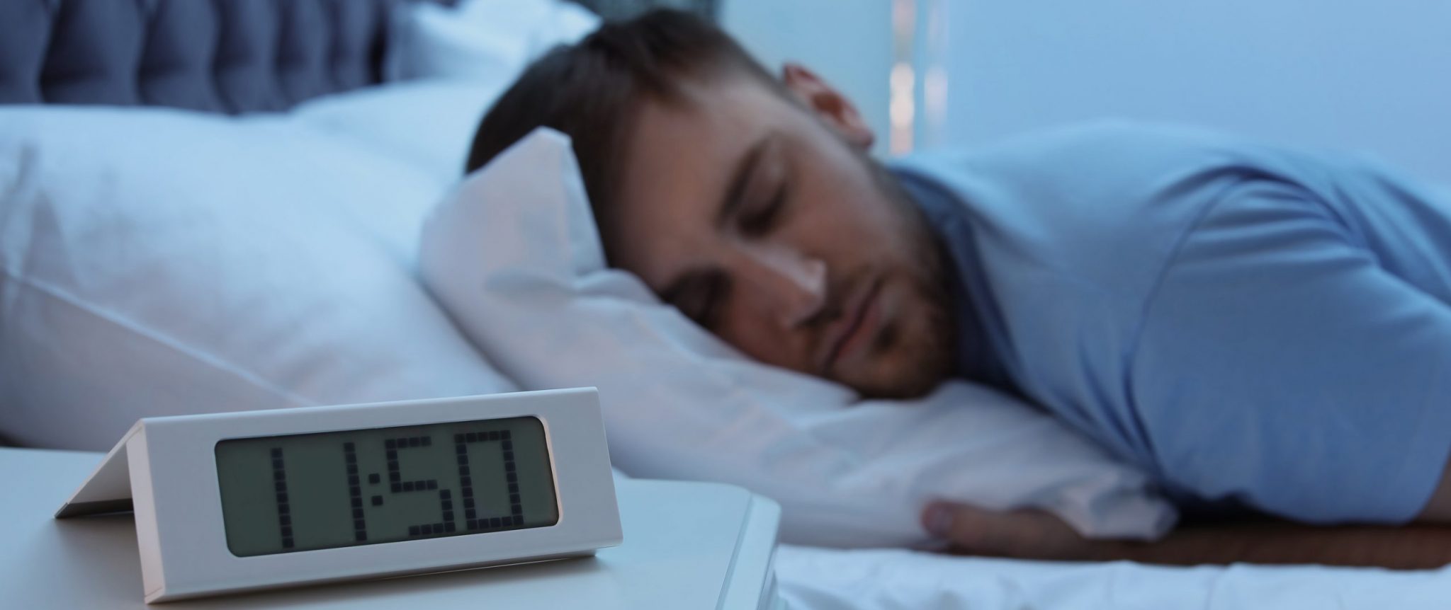 Alarm Clock On Table And Young Man Sleeping In Bed At Night Mijn